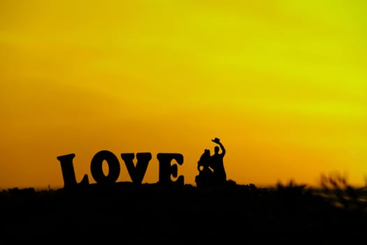 miniature people / toy photography - conceptual valentine holiday illustration. Bride and groom silhouette standing at the sand beach with love word block