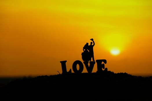 miniature people / toy photography - conceptual valentine holiday illustration. Bride and groom silhouette standing at the sand beach with love word block