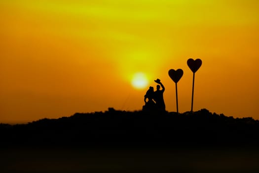 miniature people / toy photography - conceptual valentine holiday illustration. A Couple silhouette walking at the sand beach with heart balloon