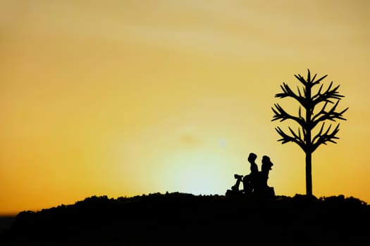 miniature people / toy photography - conceptual valentine holiday illustration. A couple silhouette riding a scooter at the sand beach with dried tree