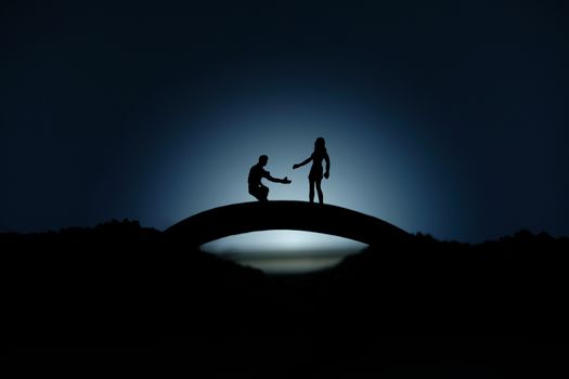 miniature people / toy photography - conceptual valentine holiday illustration. A man proposing a girl silhouette at the bridge under the moon light