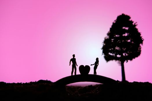 miniature people / toy photography - conceptual valentine holiday illustration. A man proposing a girl silhouette above the bridge