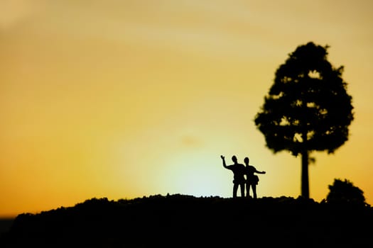 miniature people / toy photography - conceptual valentine holiday illustration. Happy couple holding each other enjoying sunset view bellow a big tree