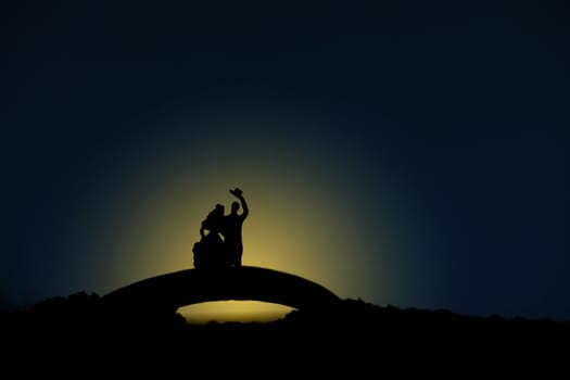 miniature people / toy photography - conceptual valentine holiday illustration. A bride and groom silhouette standing above bridge at night with moon light