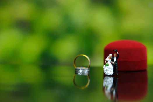 Miniature wedding concept. Bride and groom make greeting in front of red heart ring box. image photo