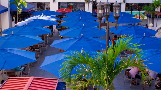 An Outdoor Shopping Area Filled With Blue Umbrealls in a Tropical Location