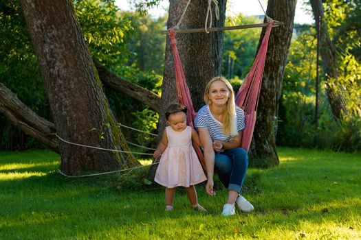 A young woman with a small child is sitting in a hammock in her garden.