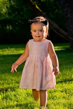 Baby girl walking on the lawn in the park.