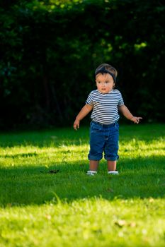 Surprised baby girl walking on the lawn in the park.