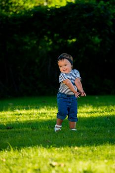 Smiling baby girl walking on the lawn in the park.