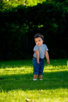 Baby girl walking on the lawn in the park.