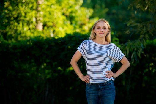 Young woman in jeans and a striped T-shirt posing in the garden.