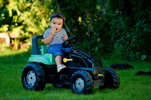 Baby girl playing with toy tractor in a garden.