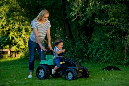 Baby girl and mother playing with toy tractor in a garden.