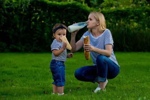 A young woman in jeans and a striped T-shirt drink milk from a glass bottle. Family picnic.