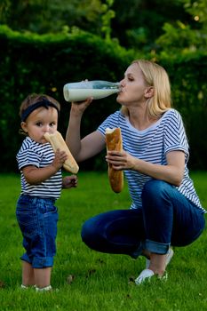 A young woman in jeans and a striped T-shirt drink milk from a glass bottle. Family picnic.