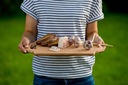 Young woman holding wooden board with garlic, lard and bread. Closeup.
