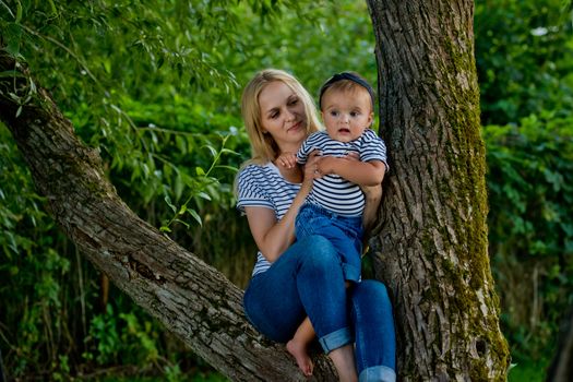 A young woman in jeans and a striped T-shirt and her little daughter are sitting on a tree.