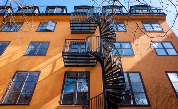 Black spiral fire escape against the wall of an orange building with large windows.