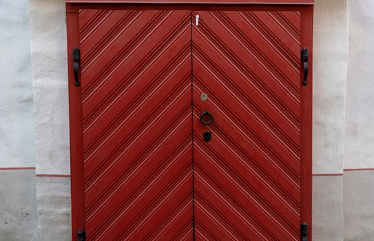 Large red wooden gate with black forged handles and hinges in an old building.