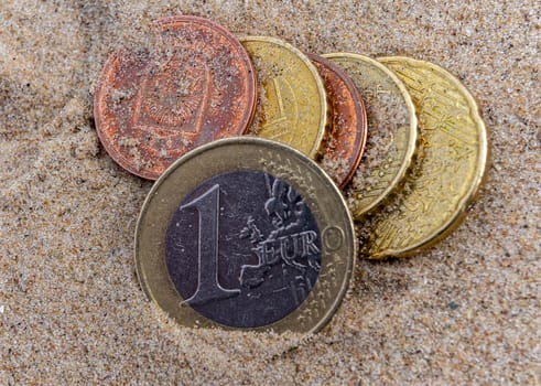 Onу euro coin on the wet fine sand of a sea beach.