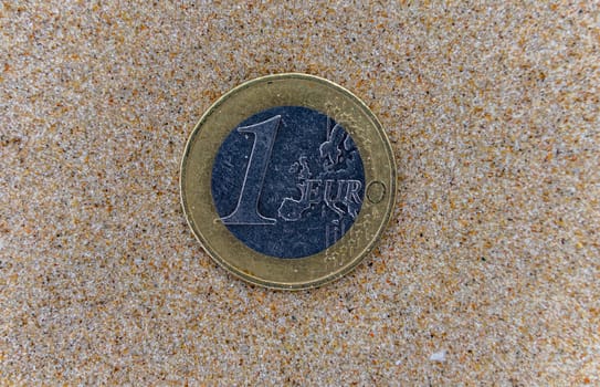 1 euro coin on the wet fine sand of a sea beach.