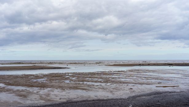 Reflection of clouds in a small lehman on the sandy shore of the Baltic Sea in Jurmala in cloudy weather.