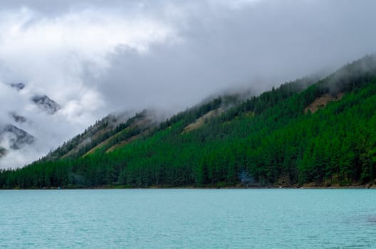 Shavlinskoye lake in the Altai Republic on the background of mountain peaks shrouded in fog.