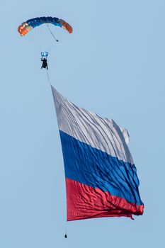 Skydiver in the sky with a giant flag of Russia against the blue sky.