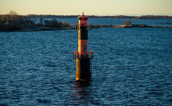 Lighthouse in the strait between the islands of the Stockholm archipelago, lit by the rays of the sun, in the early morning.