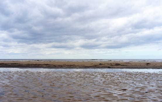 Reflection of clouds in a small lehman on the sandy shore of the Baltic Sea in Jurmala in cloudy weather.