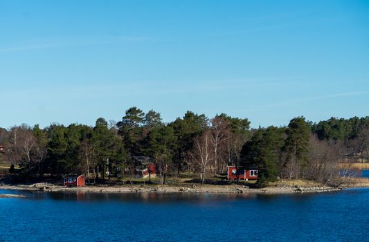 Picturesque summer houses painted in traditional falun red on dwellings island of the Stockholm archipelago in the Baltic Sea in the early morning.