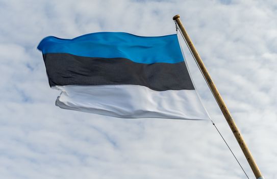 The developing white-black-blue flag of Estonia against the background of clouds in the sky.