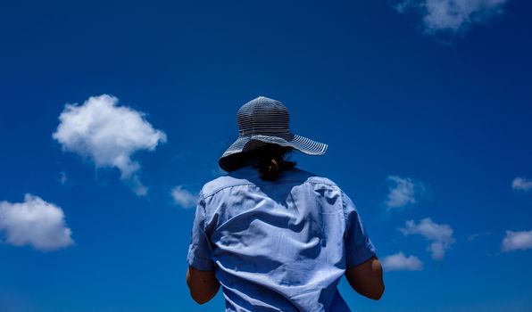 Girl in a wide-brimmed striped hat on a background of blue sky with small clouds