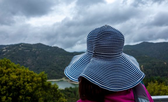 A girl in a wide-brimmed striped hat is watching the mountain landscape.