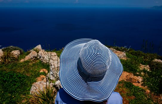 A girl in a wide-brimmed striped hat looks at the beautiful landscape of the coastline