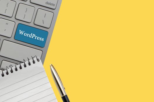 WORDPRESS text on keyboard, notepad and fountain pen over yellow background. Business and technology concept