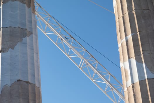 A construction crane behind old stone pillars with a bright blue sky in the background