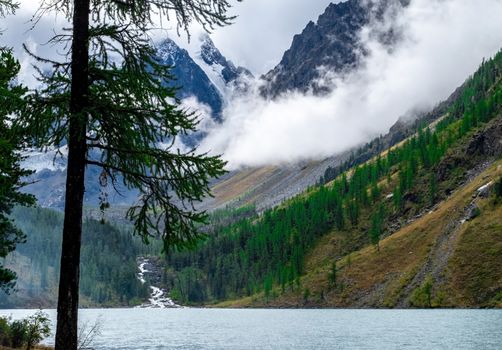 Shavlinskoye lake in the Altai Republic on the background of mountain peaks shrouded in fog.