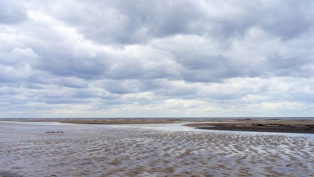 Reflection of clouds in a small lehman on the sandy shore of the Baltic Sea in Jurmala in cloudy weather.