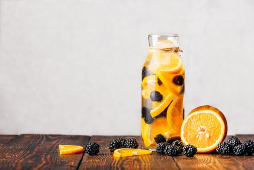 Bottle of Water Infused with Sliced Raw Orange and Fresh Blackberry. Ingredients on Wooden Table.