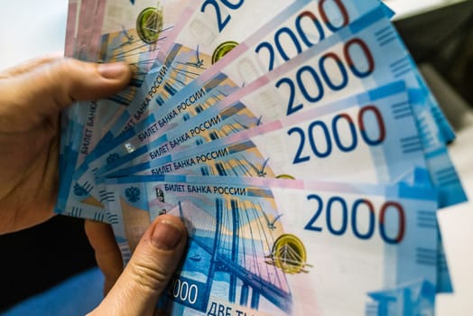A fan of banknotes of 2000 Russian rubles in the hand of a young man.