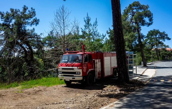 Red fire truck on a forest mountain road in the hot summer in the mountains of Central Cyprus.