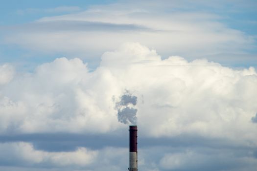 Smoke from a red-and-white pipe of a thermal power plant against a background of white clouds and blue sky