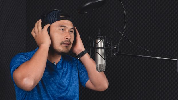Confident Asian mature young man and a microphone Practice singing in the recording studio. Artist audition for media, music, and performance producer.