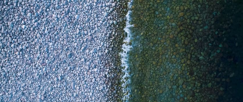 Coastline, sea wave goes ashore of stone and pebbles.