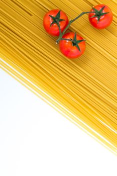 Uncooked spaghetti and cherry tomato on white background. Top view with copy space.