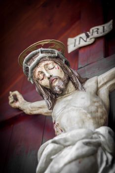 The bleeding body of Jesus Christ, crucified on a wooden cross. Shallow depth of field.