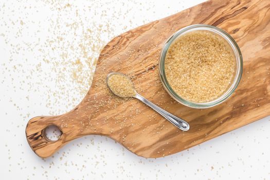 Organic brown sugar in glass jar on wooden chopping board. Top view.