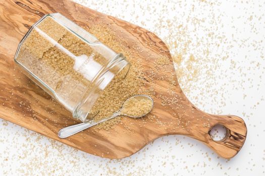 Organic brown sugar in glass jar on wooden chopping board. Top view.